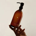 A hand holding a Kuishi Minimalist Soap Dispenser with a solid circle design, made of amber glass.
