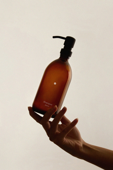 A hand holding a Kuishi Minimalist Soap Dispenser with a solid circle design, made of amber glass.